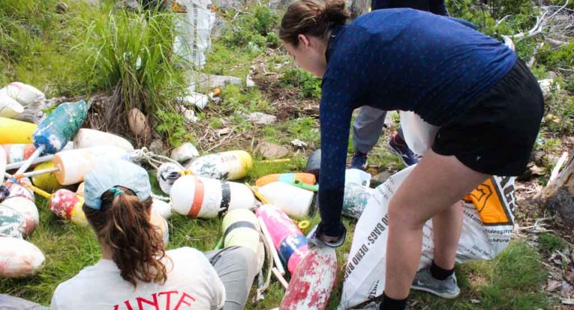 two teens pick up trash along a rocky shoreline during a service project with outward bound in maine